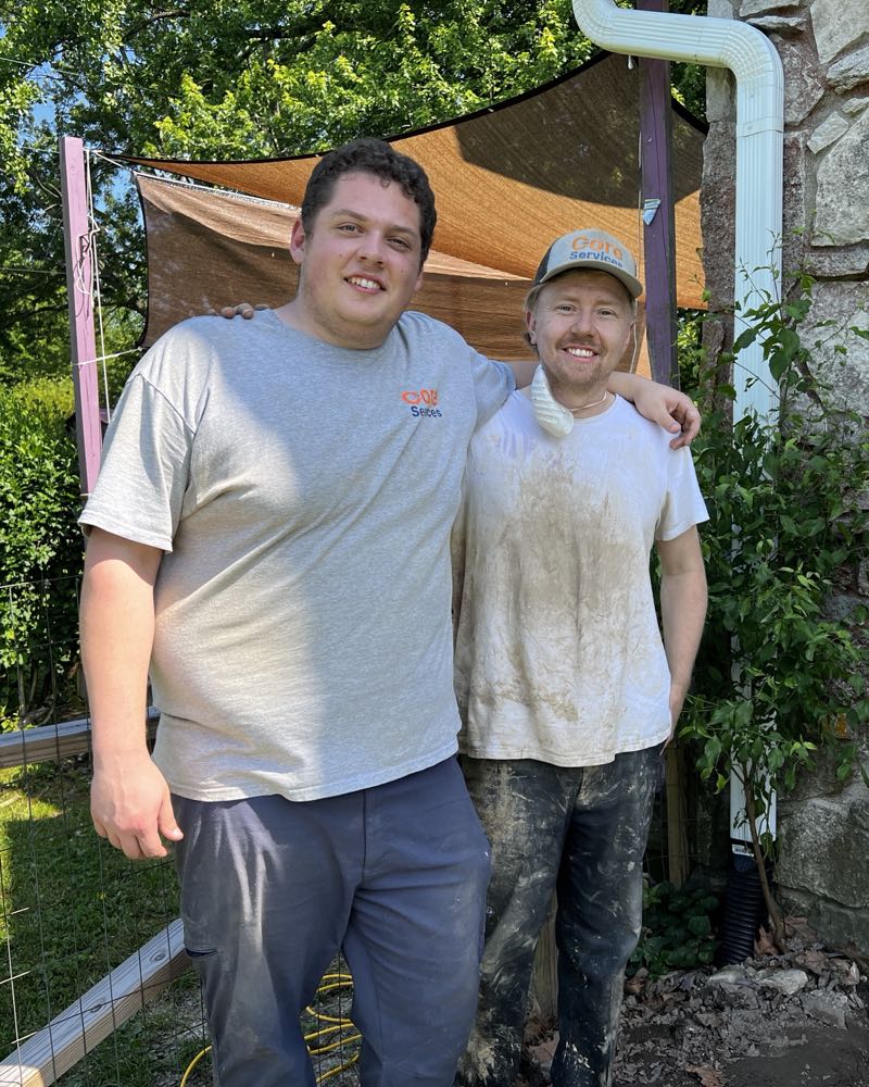 Two Core Services technicians standing together at a job site, in Core Services shirts and cap